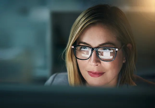 A woman looking at a computer screen with the screen reflected on her glasses.