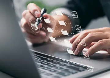 A person working on a laptop with icons appearing projected from the screen.