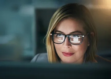 A woman looking at a computer screen with the screen reflected on her glasses.