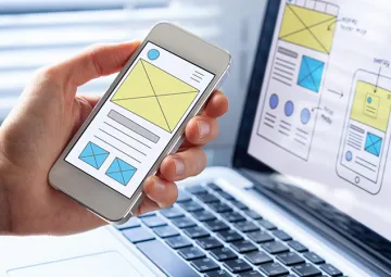 A person holding a phone next to a laptop with web design features displayed on both screens.