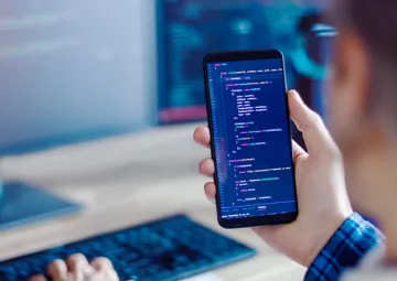 A person holding a phone with JavaScript code displayed on the screen.