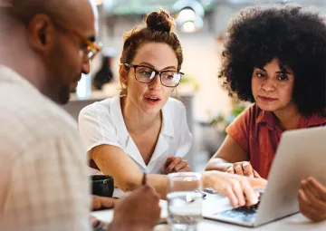 Three people looking at a laptop.